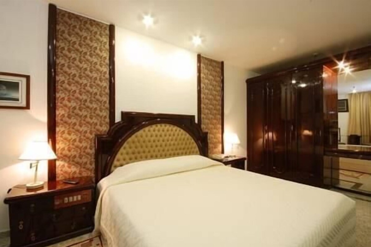 Una habitación de hotel con cama, mesitas de noche, un espejo y un armario.