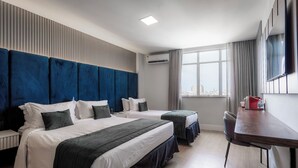 Habitación de hotel con dos camas, un escritorio, una silla, un ventanal con vista a la ciudad y un equipo de aire acondicionado.