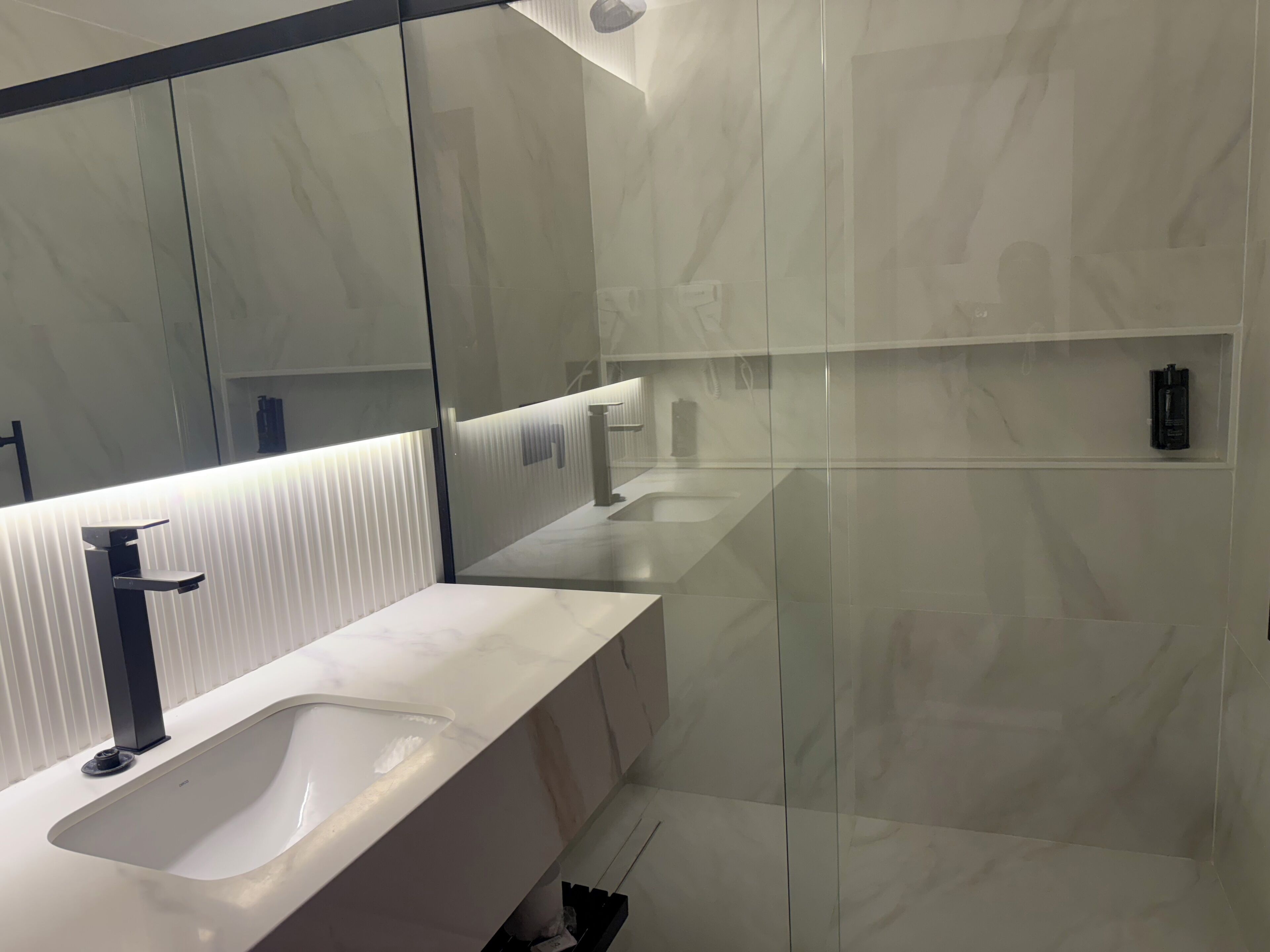 Un baño moderno con un espejo grande, dos lavamanos y una cabina de ducha de vidrio.