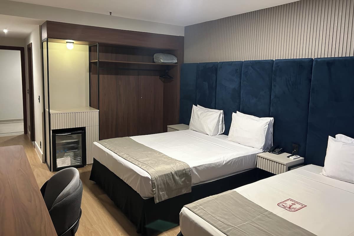 A hotel room with two beds, a desk, a wardrobe, and a small kitchenette.