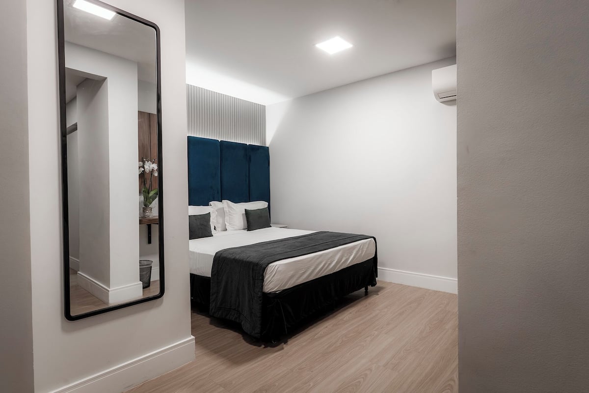 Een slaapkamer met een bed, een spiegel en een plafondlamp.