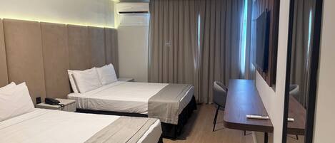 A hotel room with two beds, a desk, a chair, an air conditioning unit, and a large mirror.