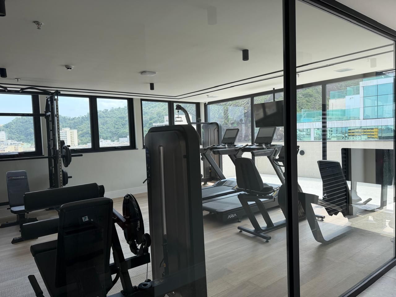 A gym with exercise equipment, large windows, and a view of a cityscape.