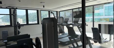 A gym with exercise equipment, large windows, and a view of a cityscape.