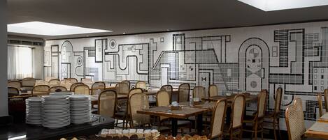 Un comedor con mesas y sillas, un bufé con diversas opciones de comida y una pared con diseños geométricos.