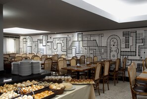 Un comedor con mesas y sillas, un bufé con diversas opciones de comida y una pared con diseños geométricos.