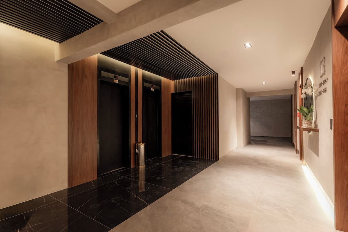 Een moderne hal met een zwart-beige betegelde vloer, houten lambrisering en een in de muur ingebouwde lift.