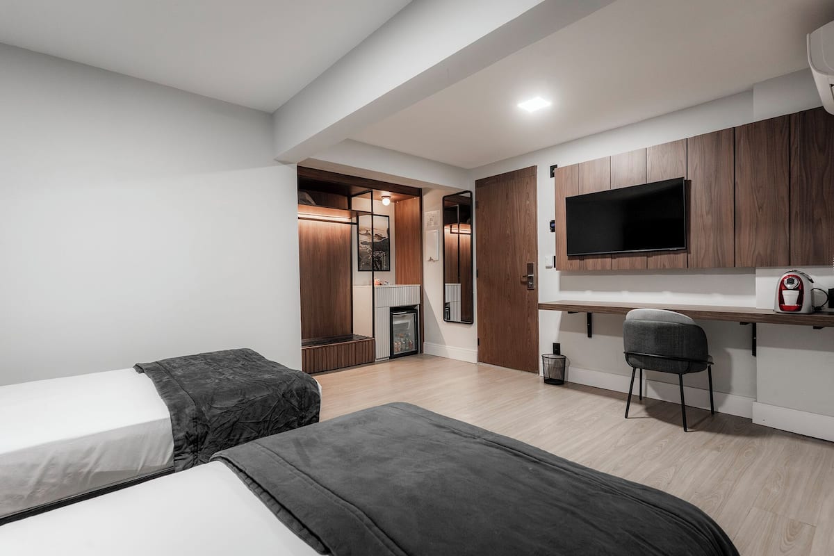 Een moderne hotelkamer met twee bedden, een kitchenette, een televisie en een klein zithoekje.