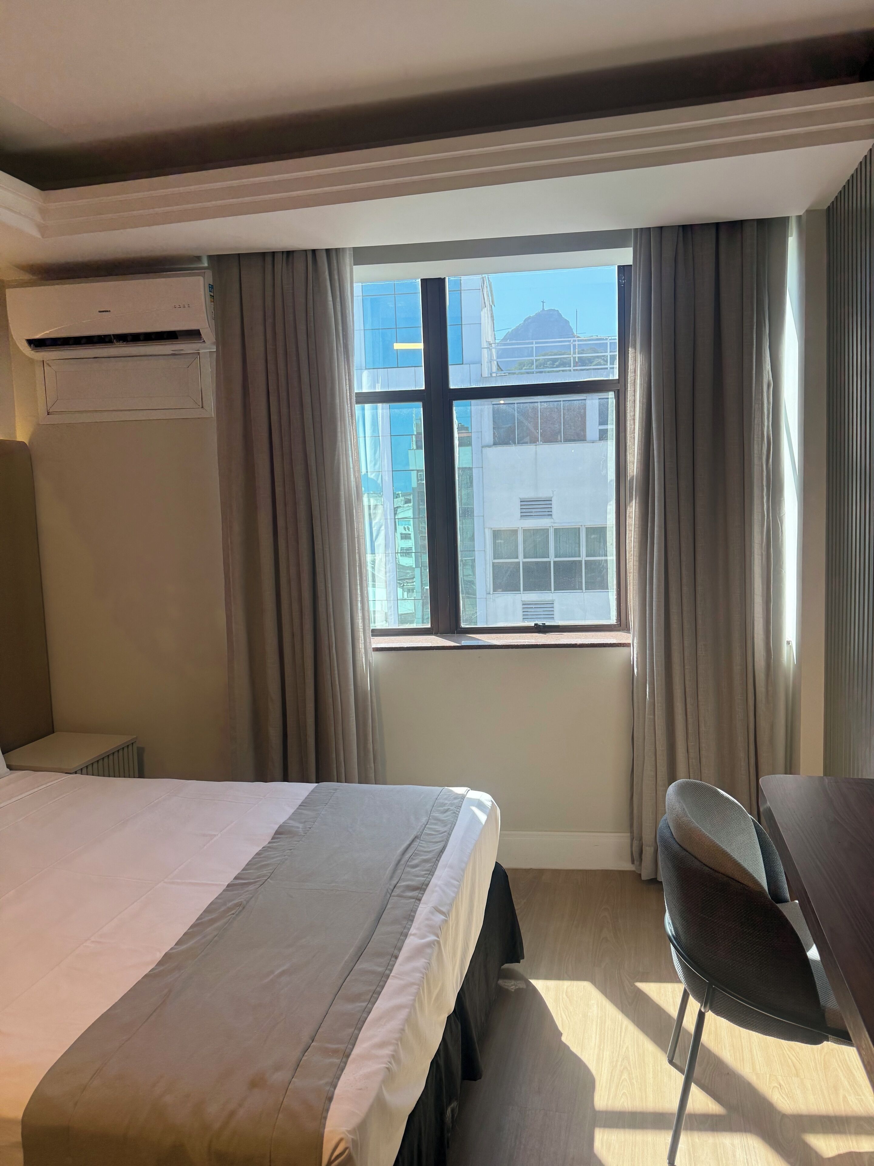 A hotel room with a bed, a desk, and a window with curtains.