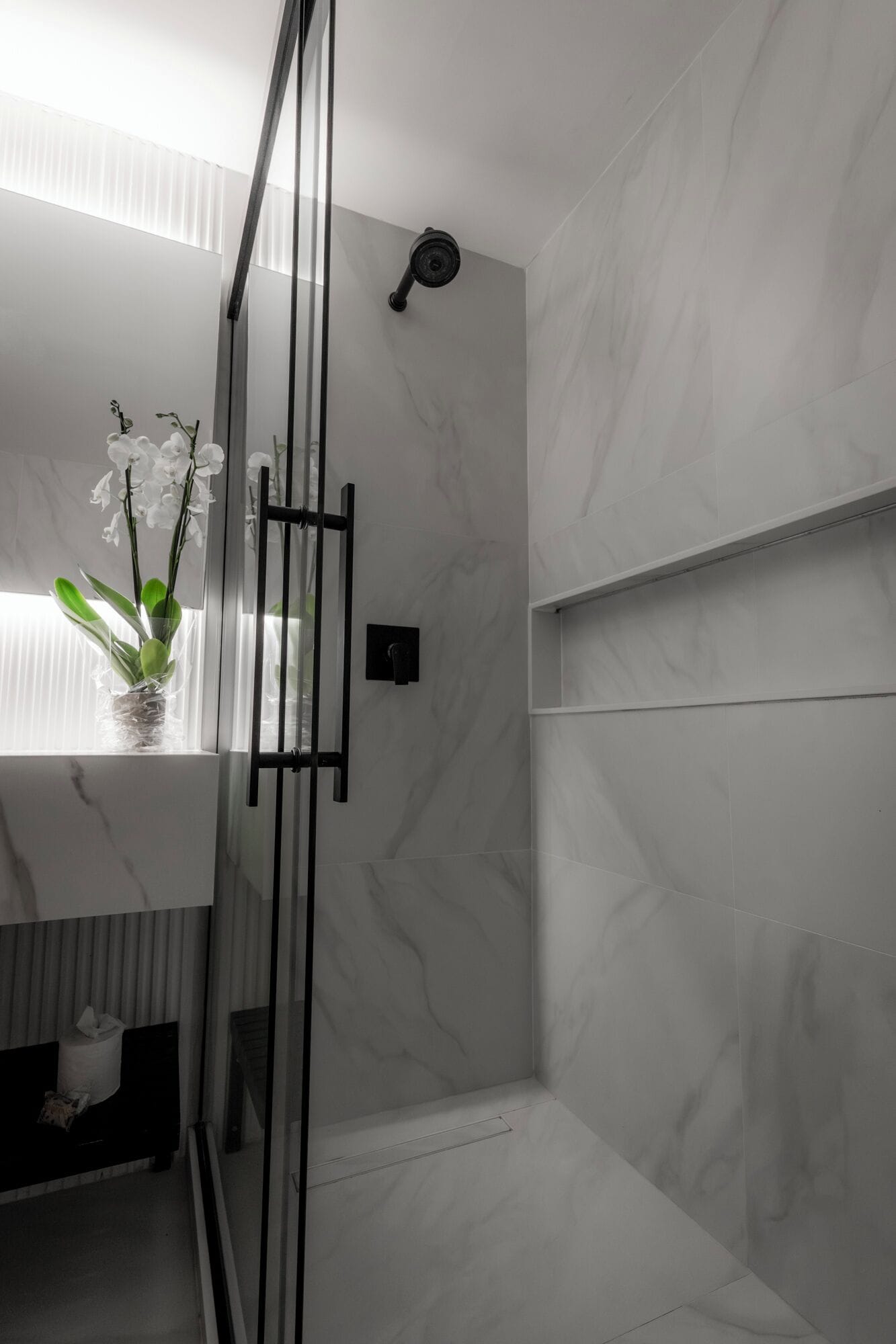 A modern bathroom with a glass shower enclosure, a marble wall, and a potted orchid.