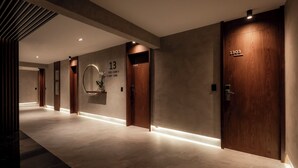 Un pasillo moderno de hotel con puertas de madera, un espejo adosado a la pared y letreros de habitaciones numeradas.