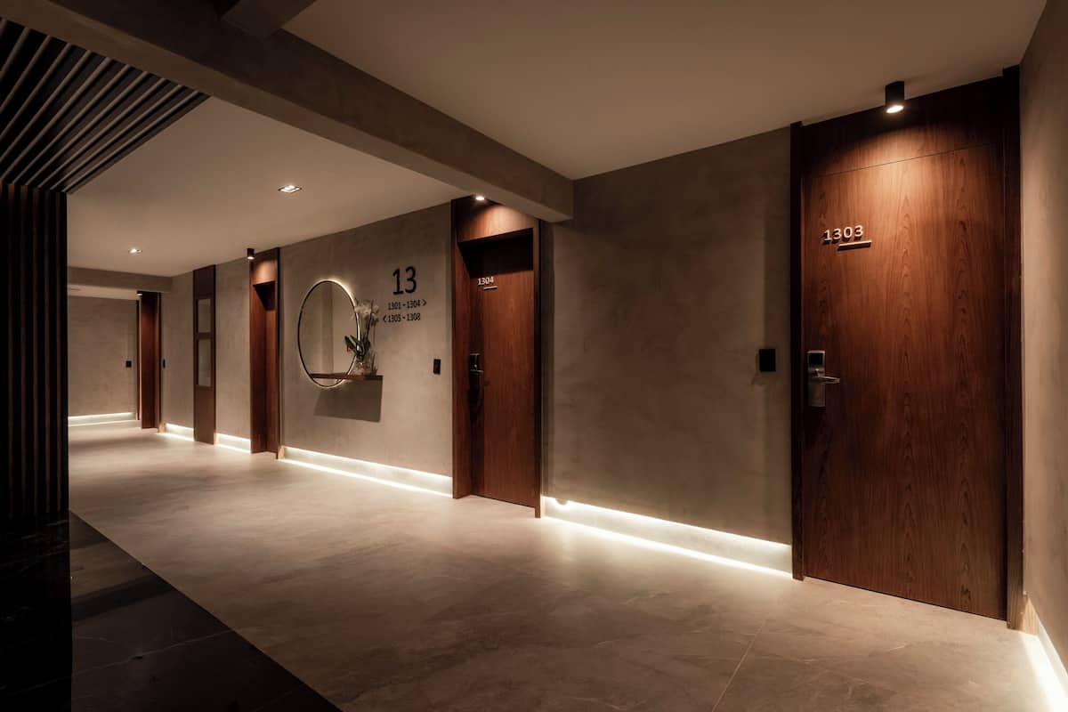 Een moderne hotelgang met houten deuren, een spiegel aan de muur en kamerdeuren met nummering.