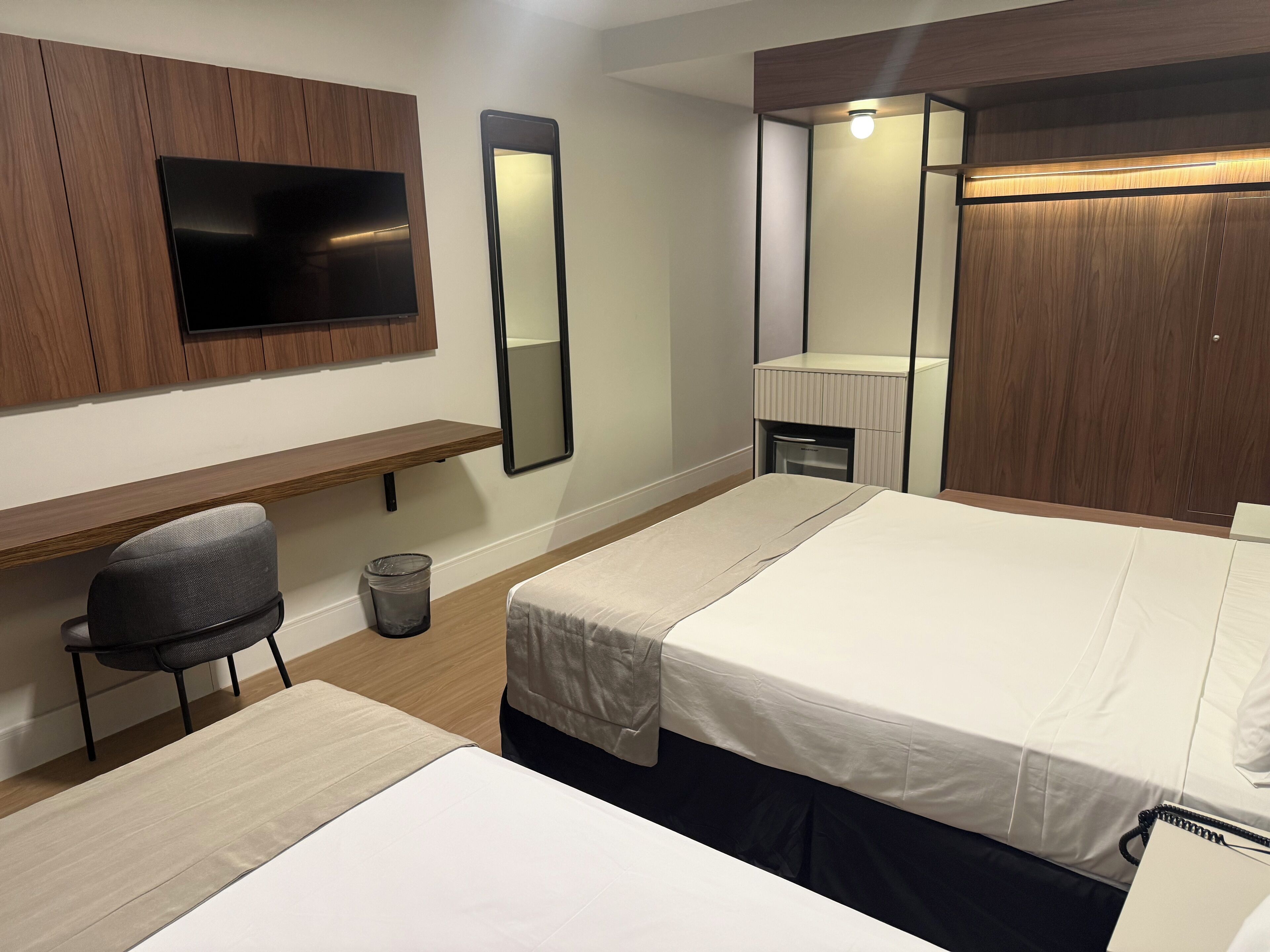 A hotel room with two beds, a desk, a chair, a mirror, and a TV.