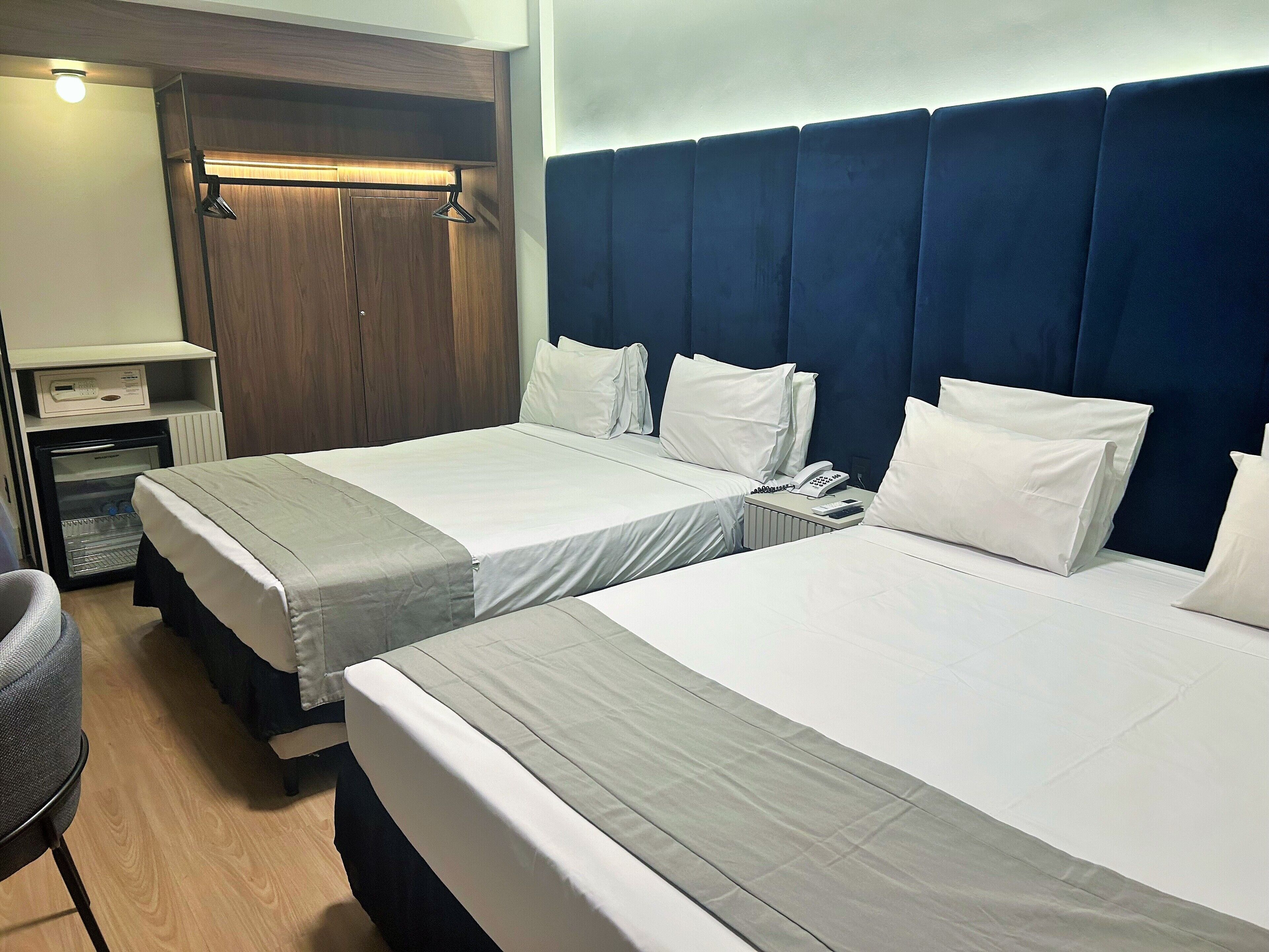 A hotel room with two beds, a desk, a chair, and a minibar.