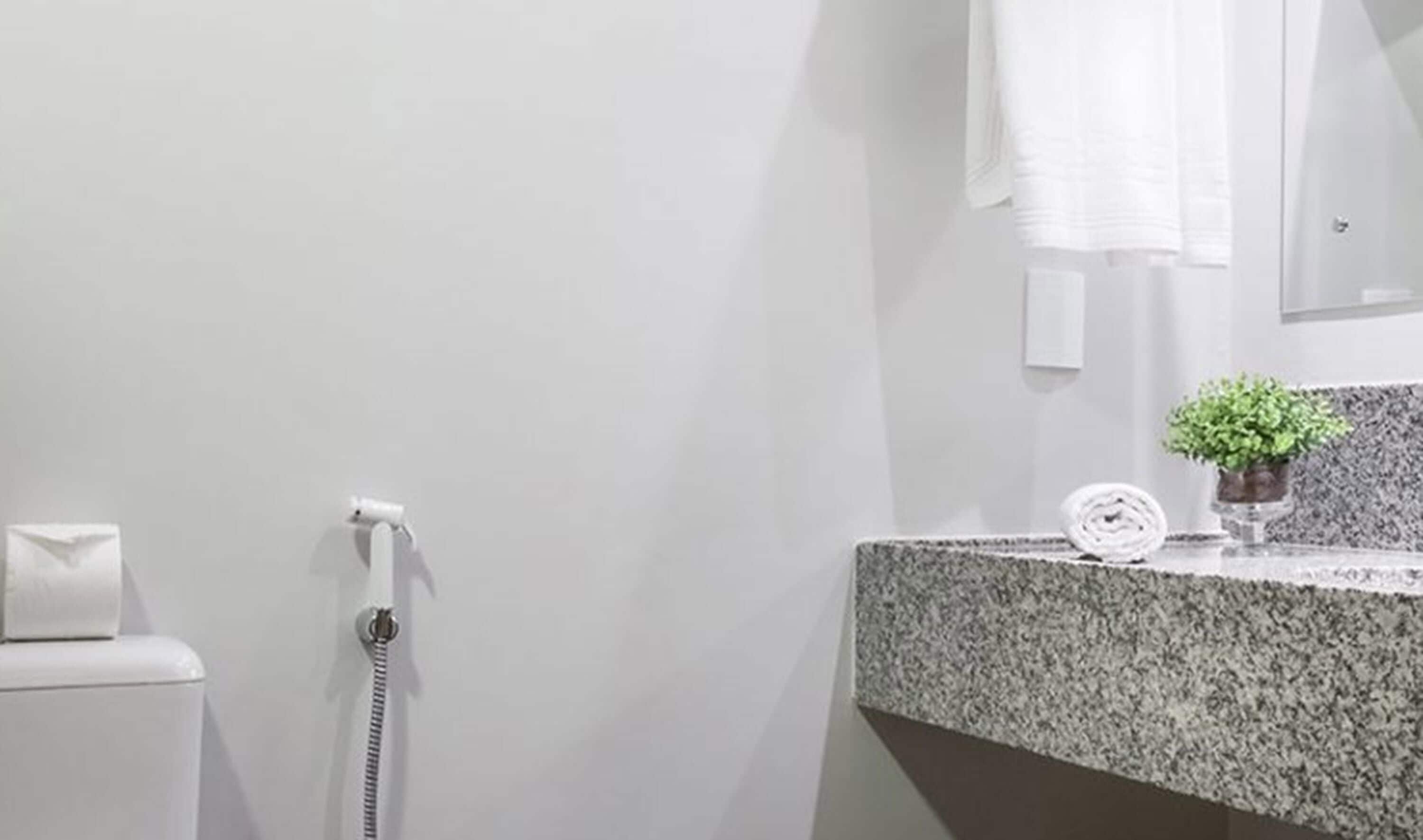 Ein Badezimmer mit Toilette, Handtuchspender, Handtrockner, einer Granit-Arbeitsplatte, einem kleinen Topf mit Pflanze und einem Spiegel.