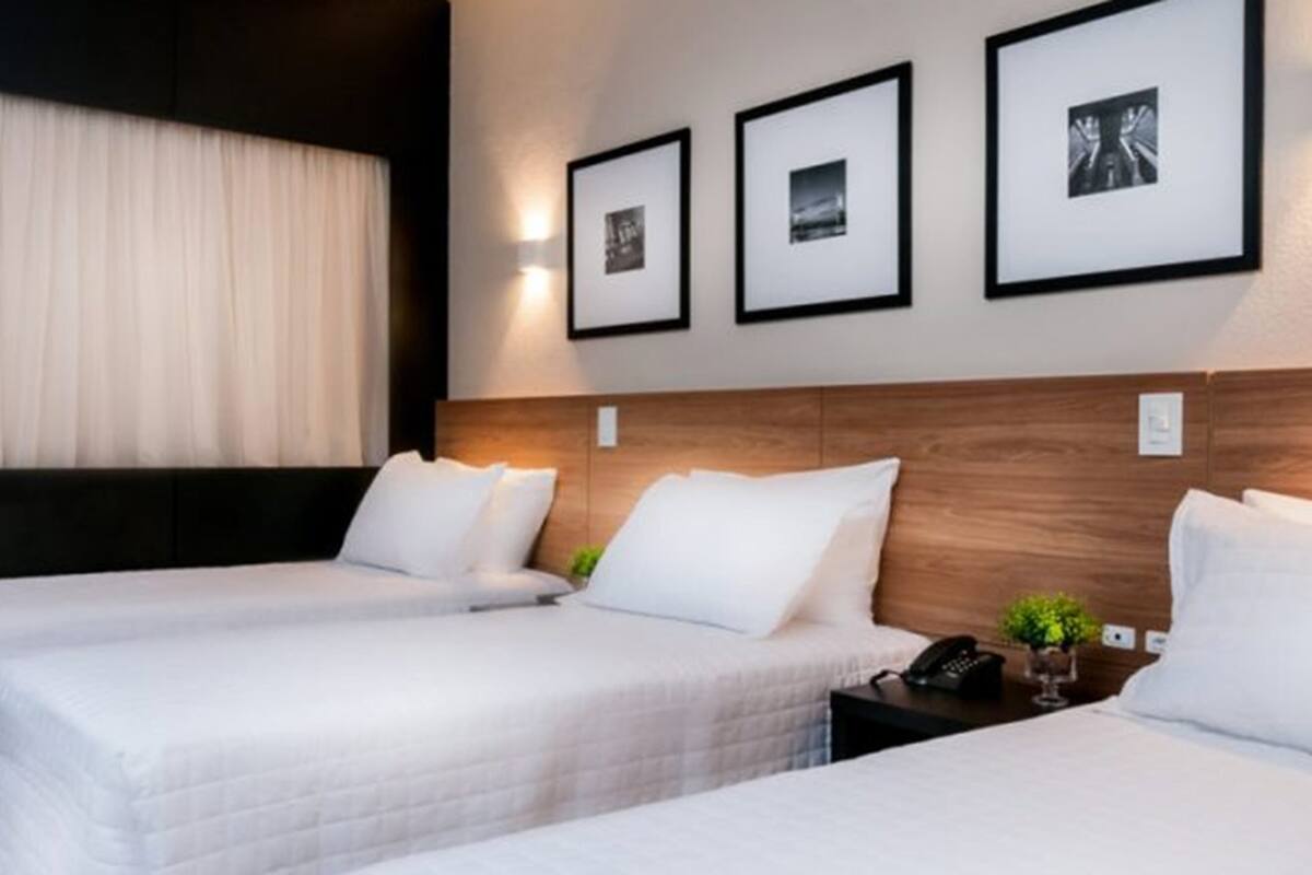 A hotel room with two beds, a wooden headboard, and three framed pictures on the wall.