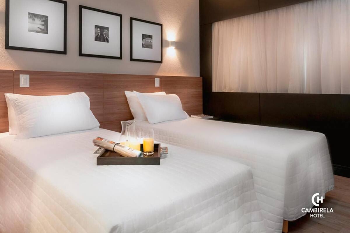 A hotel room with two beds, a tray with a newspaper, a glass of orange juice, and framed pictures on the wall.
