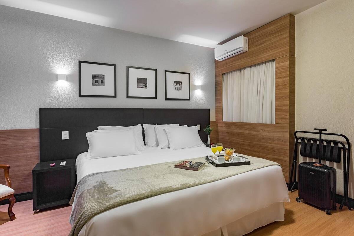 A hotel room with a bed, bedside tables, a suitcase, and framed pictures on the wall.