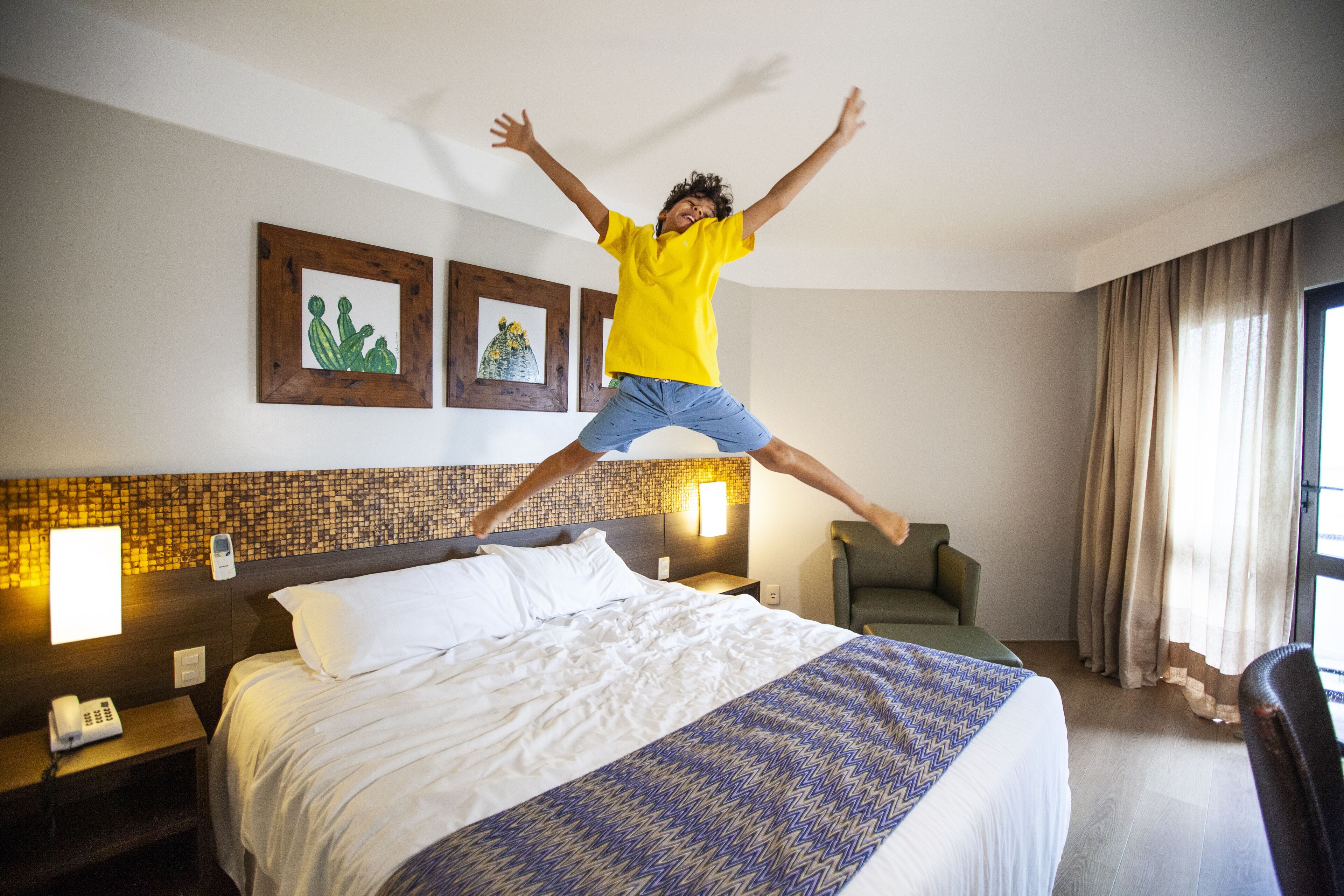 A hotel room with a bed, a nightstand, a lamp, a chair, and a window with curtains.