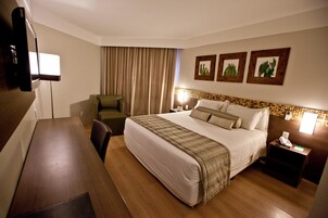 Une chambre d’hôtel avec un grand lit, un bureau, une chaise, une télévision et une table de chevet avec un téléphone.