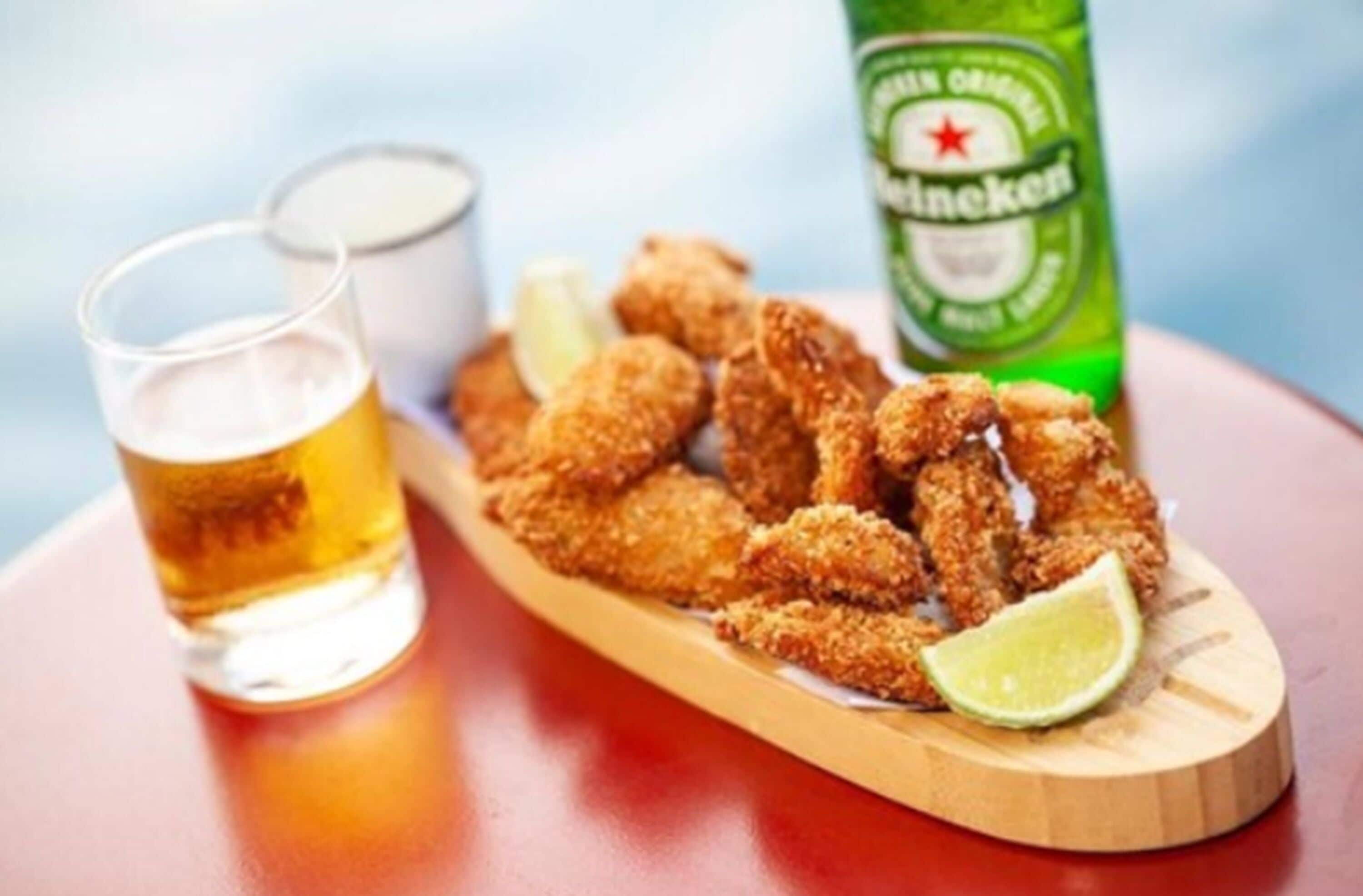 A wooden serving board with breaded chicken wings, a lime wedge, and a bottle of Heineken beer.