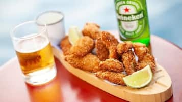 A wooden serving board with breaded chicken wings, a lime wedge, and a bottle of Heineken beer.