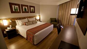 A hotel room with a large bed, a desk, a chair, and a TV.