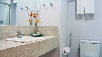 A modern bathroom with a granite countertop sink, a toilet, and a shower.