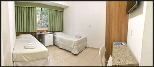 A small, clean room with two beds, a small desk, and a window with curtains.