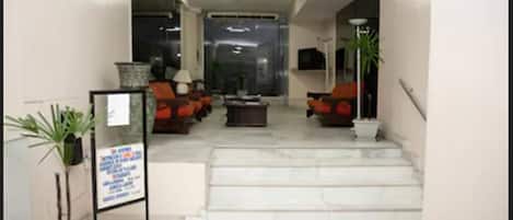 A hotel lobby with a reception desk, seating area, and a staircase leading to the upper floor.