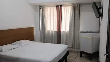 Quarto de hotel com cama, escrivaninha, televisão e janela com cortinas.