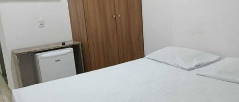 Un dormitorio con una cama, un armario de madera, un escritorio pequeño con una computadora y un televisor montado en la pared.