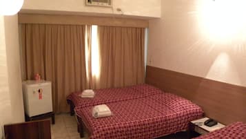 Quarto de hotel com duas camas, uma pequena escrivaninha, frigorífico e janela com cortinas.