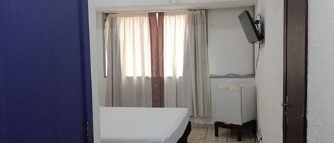 A hotel room with a bed, a desk, an air conditioning unit, and a television.