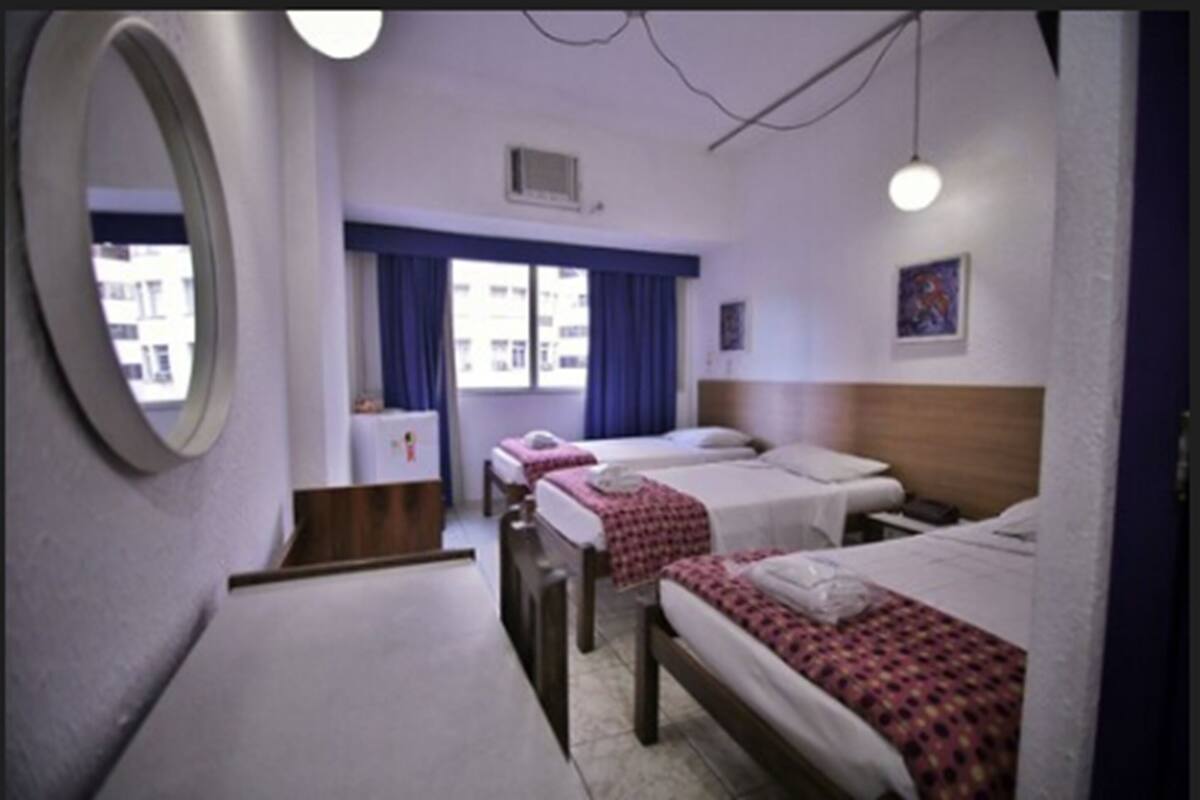 A hotel room with two beds, a small desk, a mirror, and a window with curtains.
