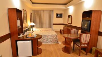 A hotel room with a bed, a small refrigerator, a table with chairs, a TV, and a mirror.