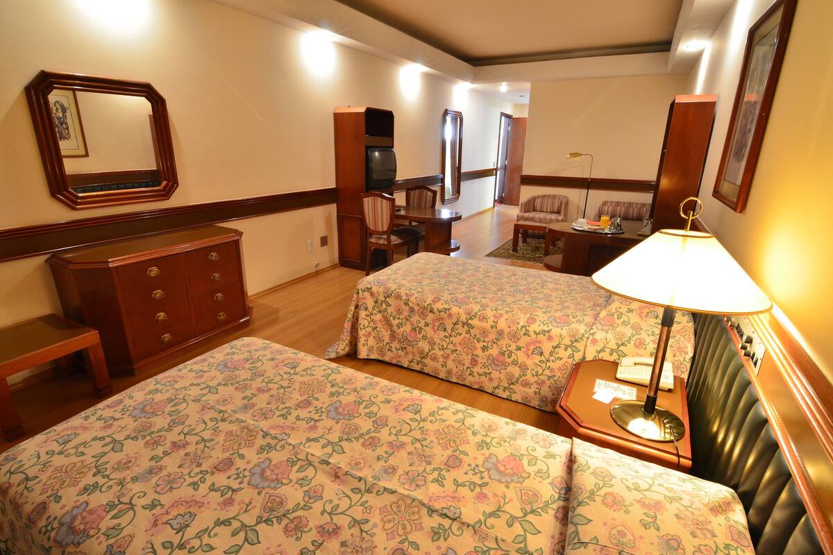 Ein Hotelzimmer mit zwei Betten, einem Schminktisch, einem Schreibtisch mit Stuhl, einem Fernseher und einer Lampe.
