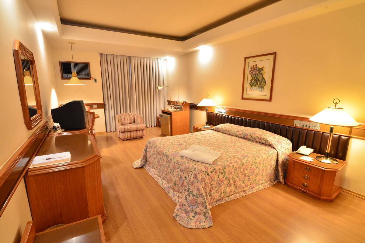 Ein Hotelzimmer mit Bett, Schreibtisch, Stuhl, Nachttisch und Spiegel.