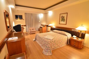 Una camera d'albergo con un letto, una scrivania, una sedia, un comodino e uno specchio.