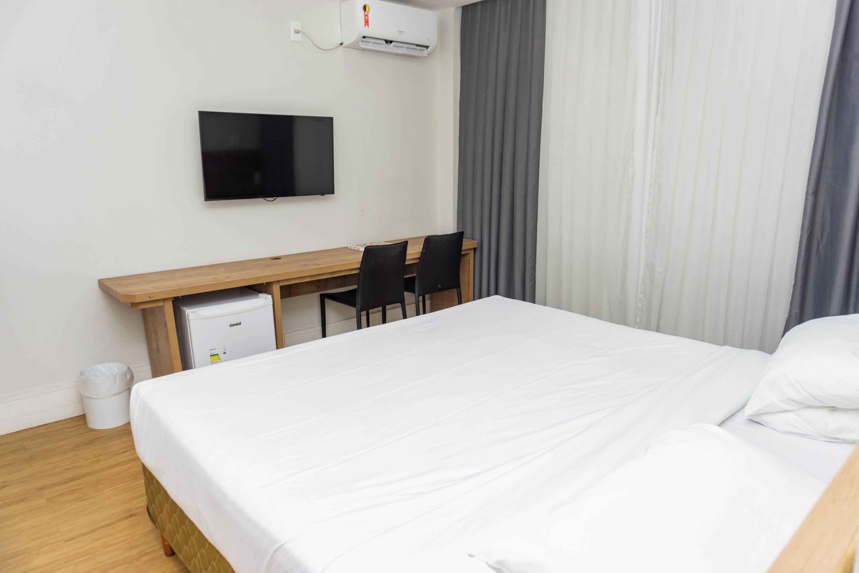 Habitación de hotel con cama, escritorio con dos sillas, televisión y aire acondicionado.