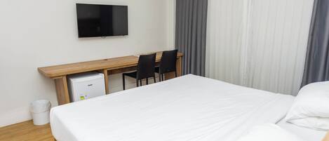Habitación de hotel con cama, escritorio con dos sillas, televisión y aire acondicionado.