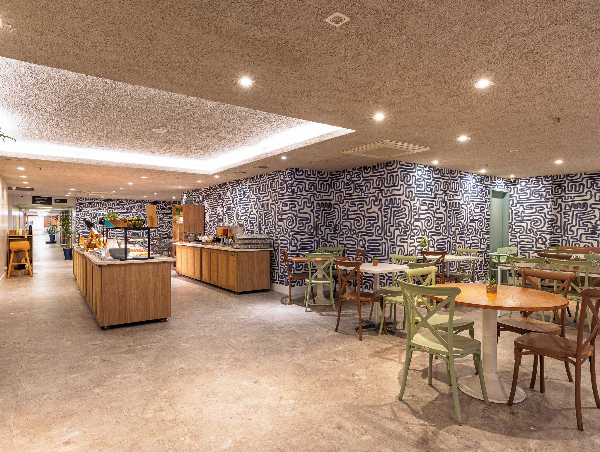 A modern cafe with a patterned wall, wooden counter, and green chairs.