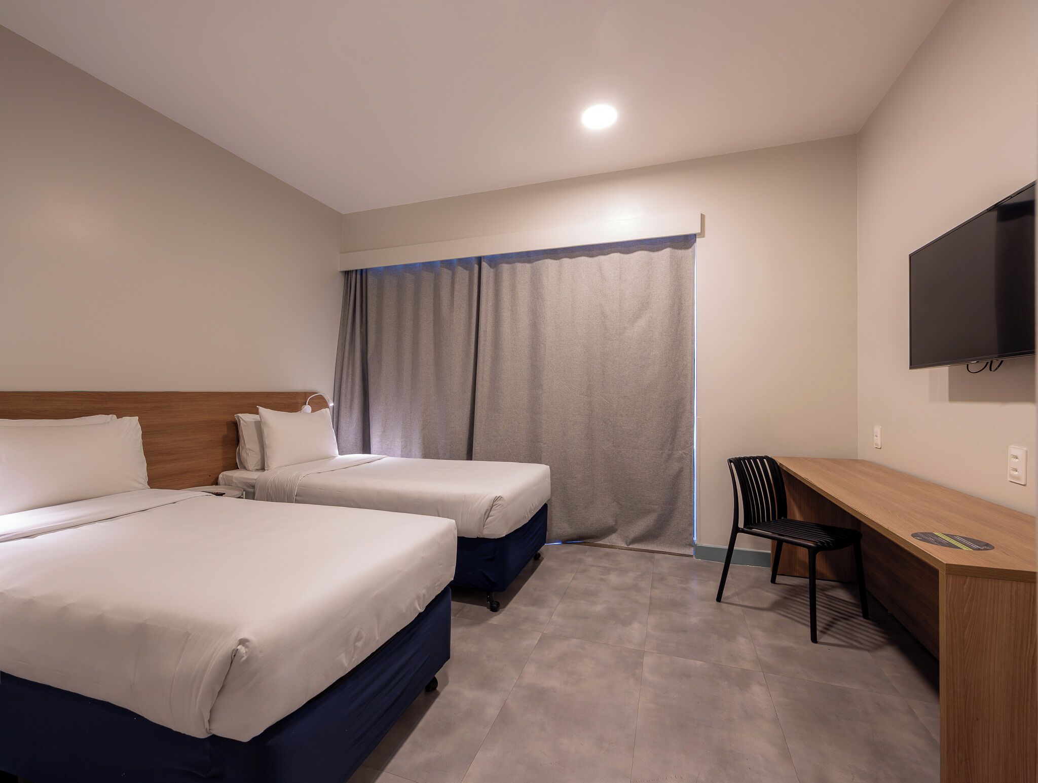 Habitación de hotel con dos camas, un escritorio, una silla, un televisor y una cortina.