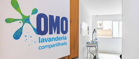 Señal que dice "OMO lavandería compartilhada" y un interior moderno con un tendedero de metal y una silla.