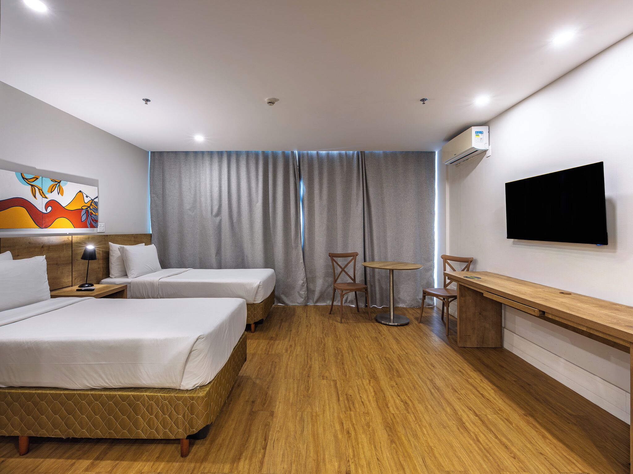 A hotel room with two beds, a desk, a chair, a TV, and a painting on the wall.