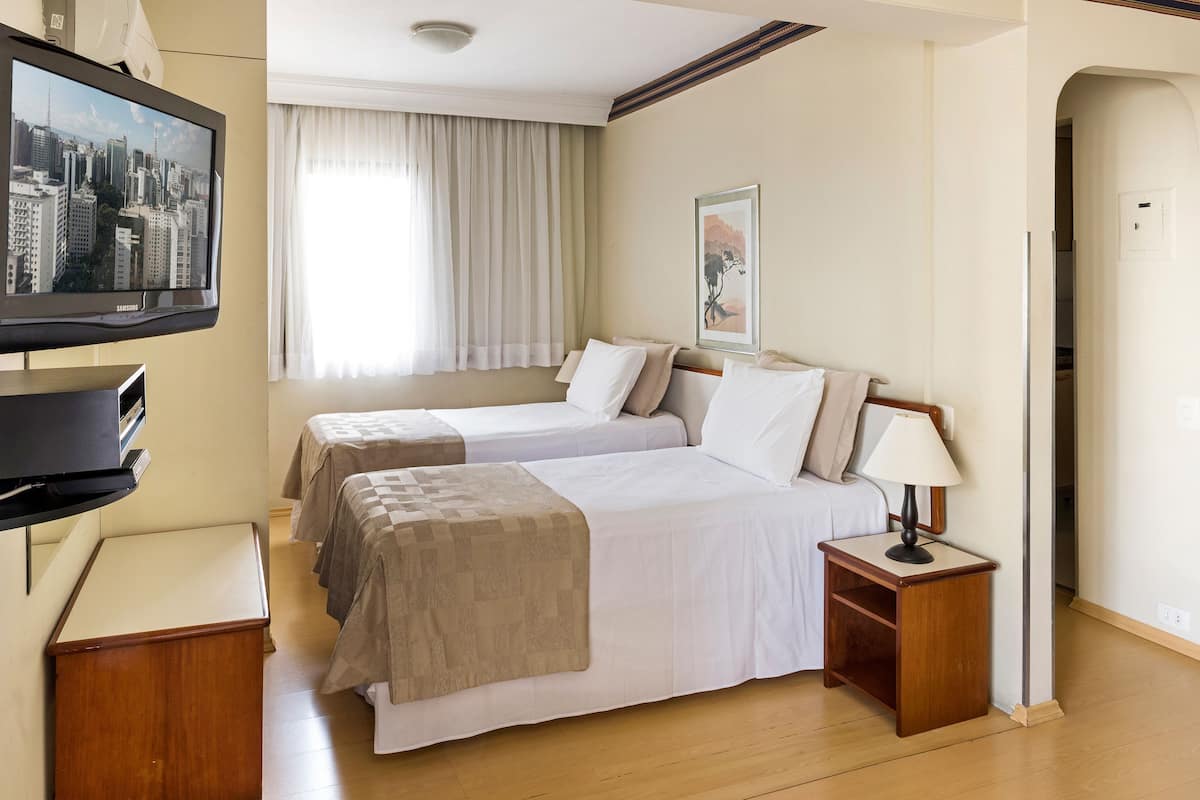 Een hotelkamer met twee bedden, een televisie, een nachtkastje met een lamp en een raam met gordijnen.