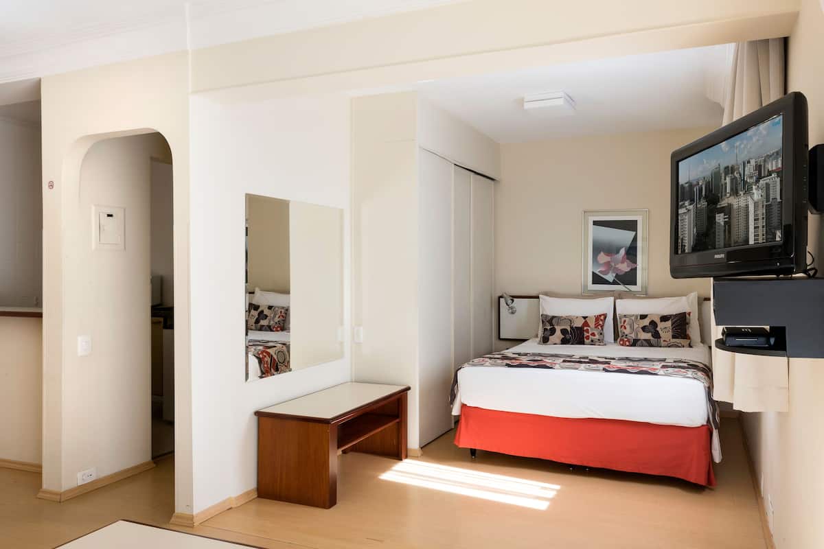 Een hotelkamer met een bed, een bureau, een spiegel, een televisie en een deur naar een andere kamer.