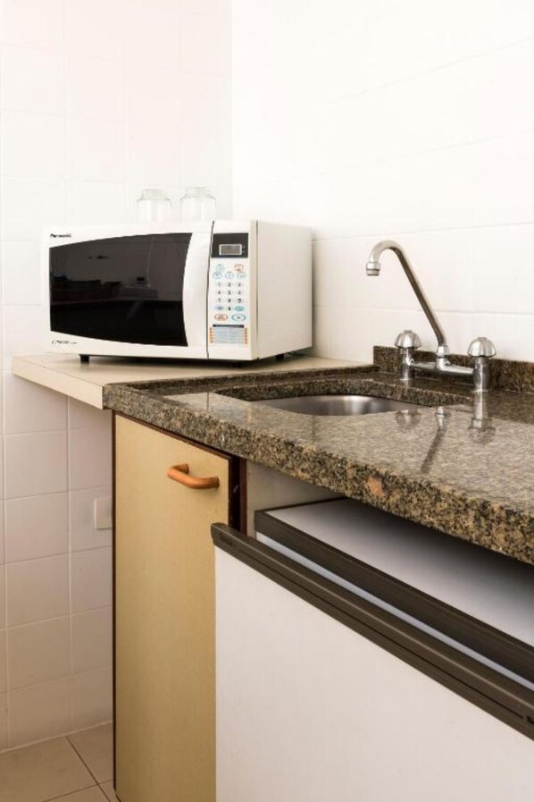 A kitchen with a built-in microwave, a stainless steel sink, and a granite countertop. - Central Park Jardins (São Paulo)