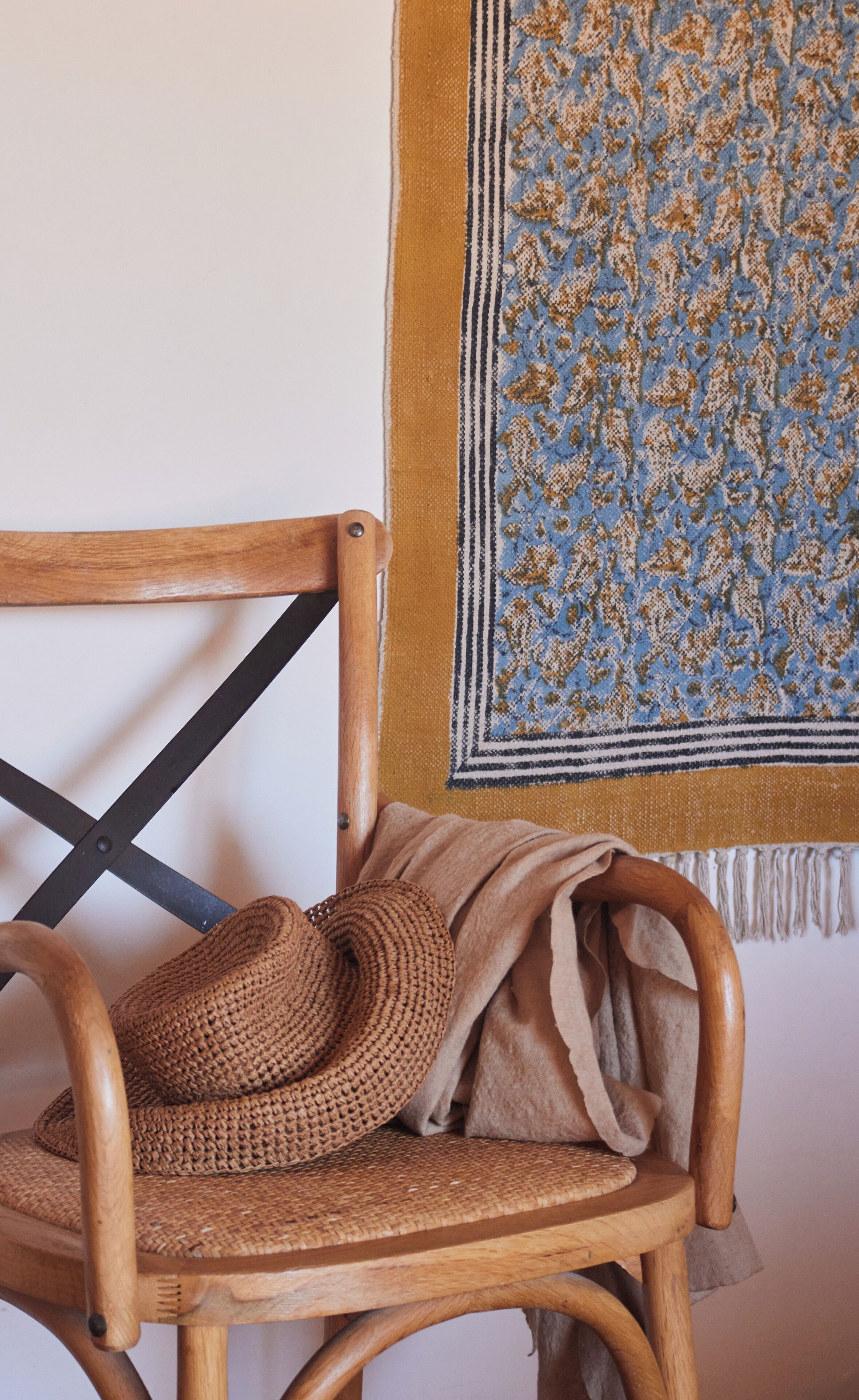 Una silla de madera con un cojín tejido y una manta estampada colgada en la pared.