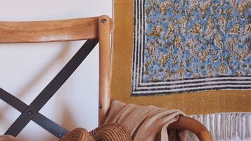 Una silla de madera con un cojín tejido y una manta estampada colgada en la pared.